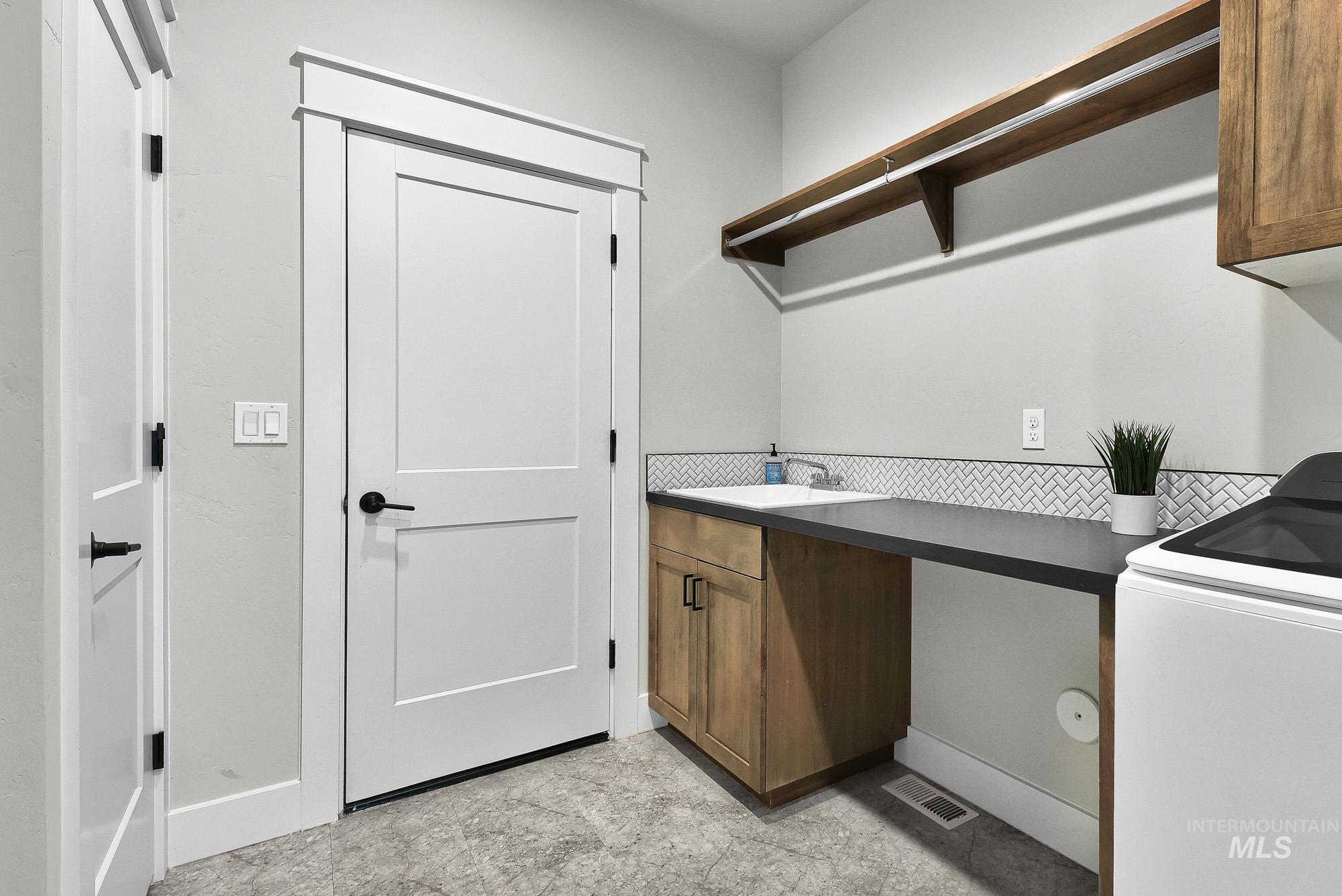 5676 East Zaffre Ridge Street Boise, ID 83716 - Photo 42 of 50 Laundry room featuring a utility sink, wood-finish cabinetry, dark countertop, and herringbone tile backsplash