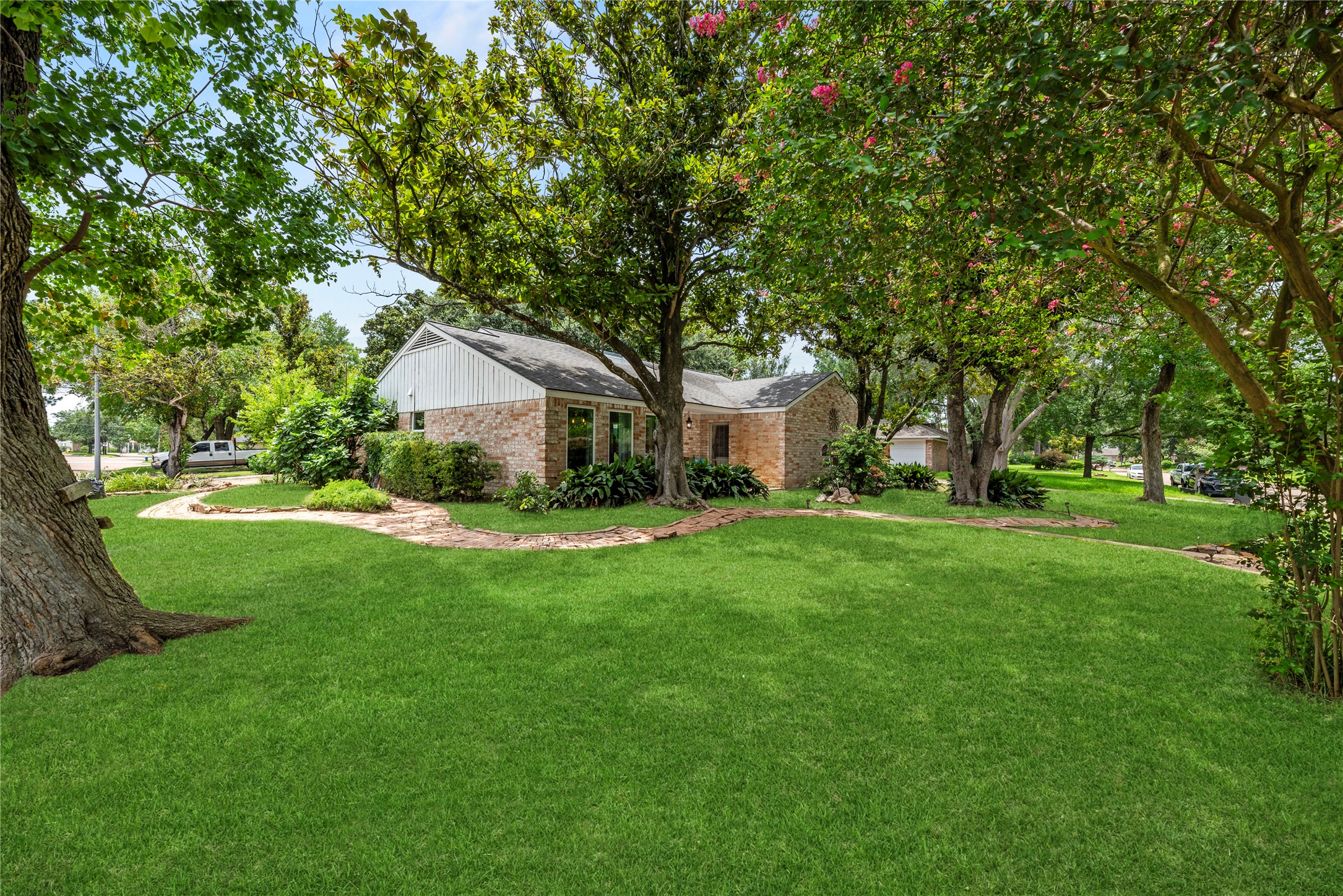 14203 Wickersham Lane Houston, TX 77077 - Photo 19 of 25 Wide-angle view of the deep front lot and side profile, emphasizing the extensive wrap-around brick accents, mature trees including a flowering crepe myrtle, and the generous property footprint.