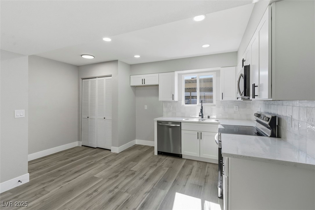 3517 Rio Robles Drive, Unit D North Las Vegas, NV 89030 - Photo 13 of 35 Kitchen featuring appliances with stainless steel finishes, white cabinetry, tasteful backsplash, light wood finished floors, and light stone countertops