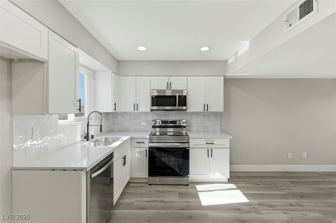 3517 Rio Robles Drive, Unit D North Las Vegas, NV 89030 - Photo 16 of 35 Kitchen featuring appliances with stainless steel finishes, tasteful backsplash, white cabinets, recessed lighting, and light stone countertops