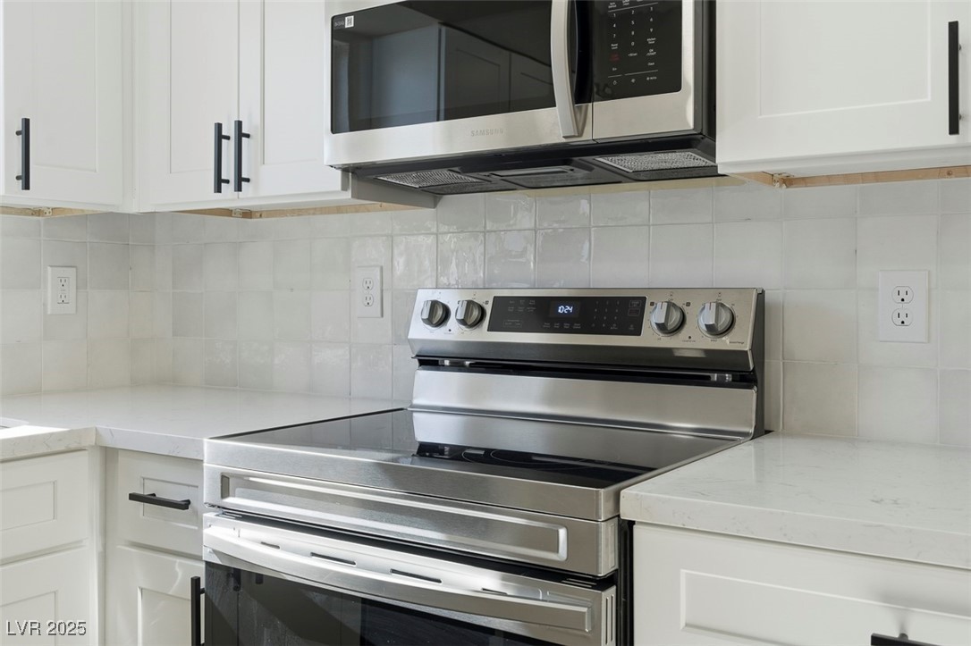 3517 Rio Robles Drive, Unit D North Las Vegas, NV 89030 - Photo 18 of 35 Kitchen featuring appliances with stainless steel finishes, white cabinets, light stone counters, and decorative backsplash