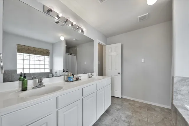 a bathroom with double sink a large mirror and a light fixture