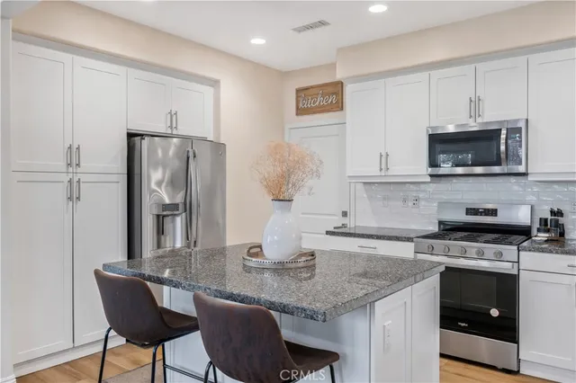 a kitchen with stainless steel appliances granite countertop a kitchen island a stove a microwave a refrigerator and cabinets