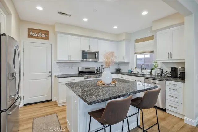 a kitchen with kitchen island granite countertop a table chairs microwave and refrigerator