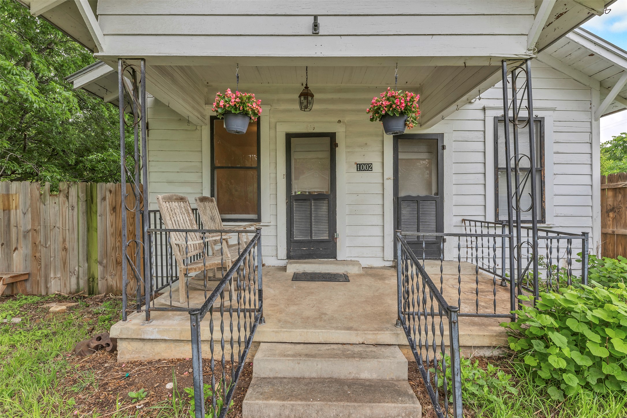 1002 Washburn Street Taylor, TX 76574 - Photo 4 of 29 The property features a front porch with concrete steps and wrought iron railings, along with white siding and dark-colored screen doors