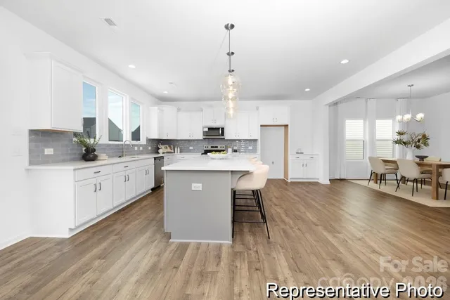 a kitchen with stainless steel appliances kitchen island granite countertop a stove a sink a refrigerator and white cabinets with wooden floor