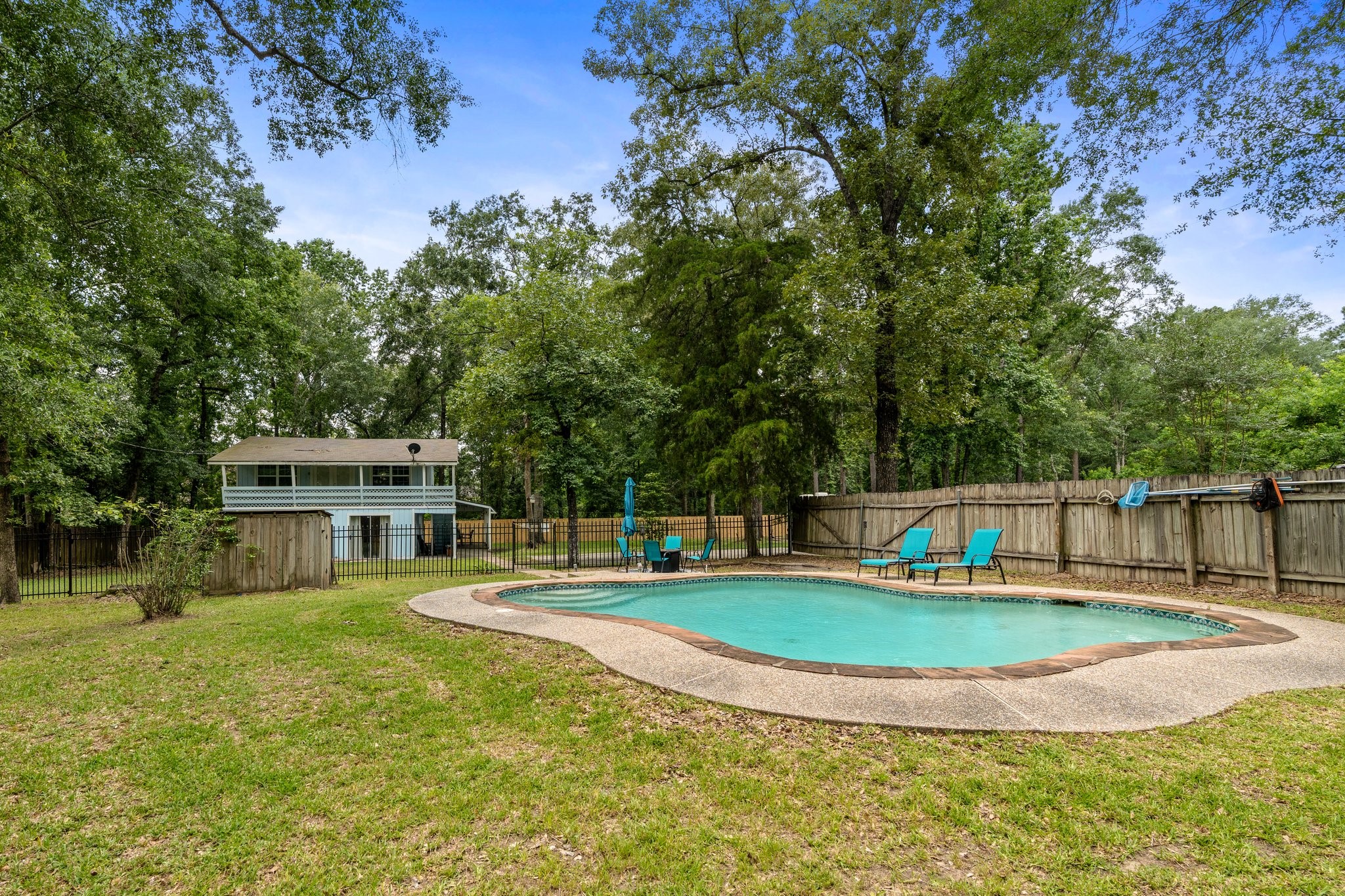 14758 Kirbee Drive Conroe, TX 77302 - Photo 3 of 35 This backyard features a spacious, fenced area with a kidney-shaped pool surrounded by greenery, offering a serene and private setting. The two-story home in the background adds extra space and functionality. Perfect for relaxation and entertaining.