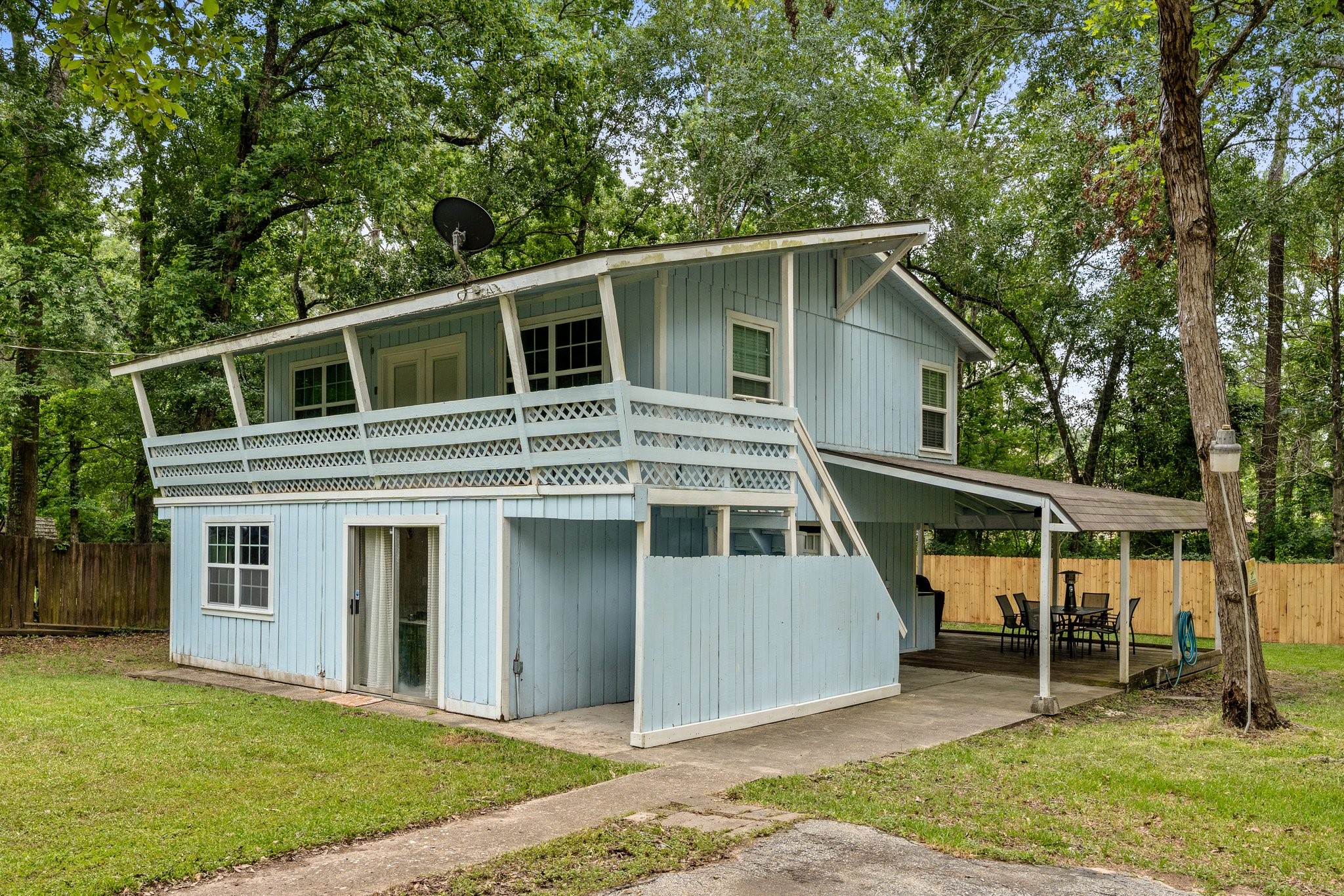 14758 Kirbee Drive Conroe, TX 77302 - Photo 4 of 35 This charming two-story home features a light blue exterior with a wraparound balcony and covered patio area. Set against a backdrop of lush trees, it offers a spacious fenced yard, perfect for outdoor activities and entertaining.