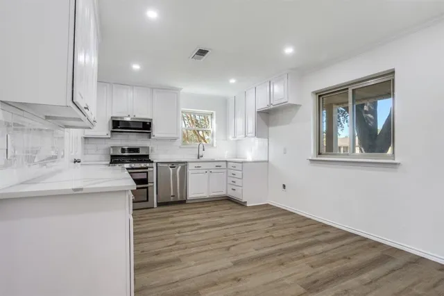 a kitchen with stainless steel appliances kitchen island granite countertop a stove a sink and white cabinets