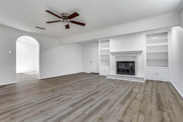an empty room with wooden floor a fireplace a ceiling fan and a window