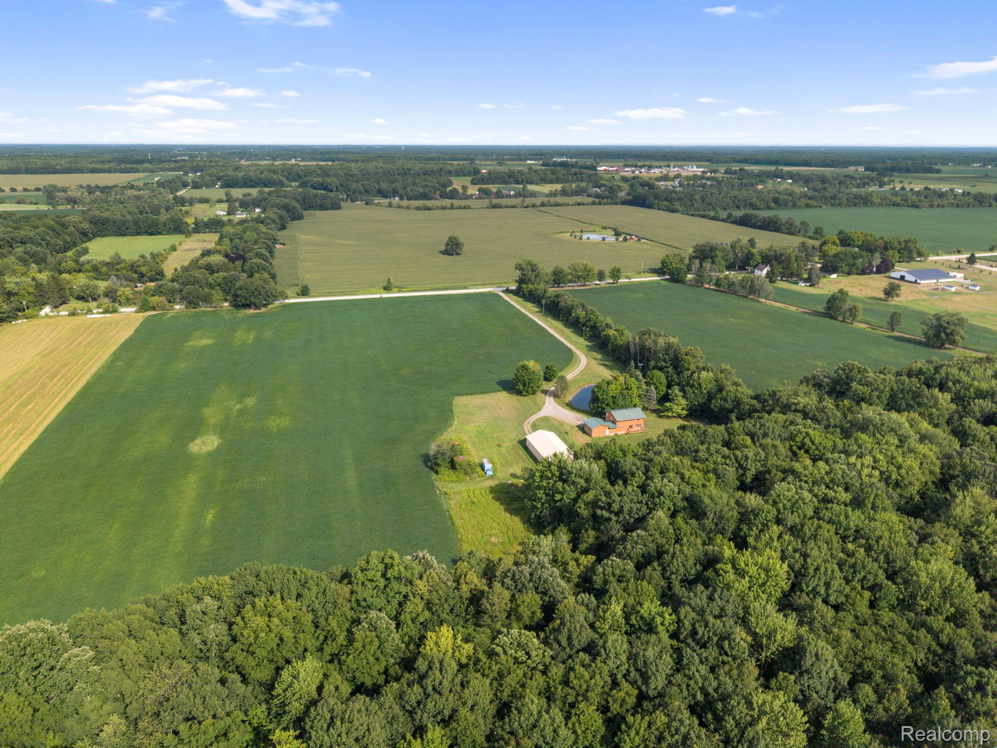 76565 McFadden Road Armada, MI 48005 - Photo 91 of 95 Expansive rural property featuring cultivated fields, wooded areas, and a visible structure with a white-domed building
