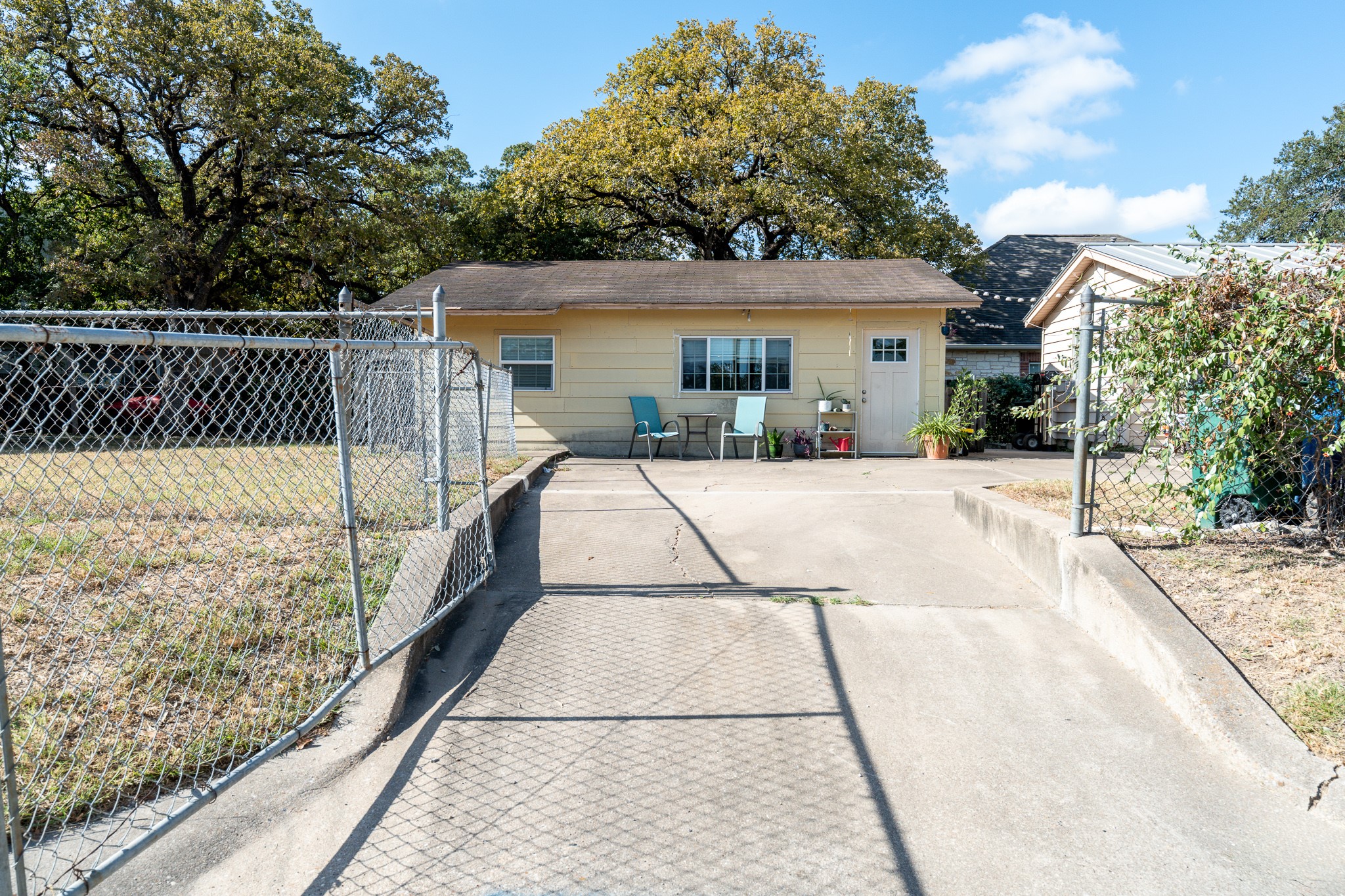 701 Vargas Road Austin, TX 78741 - Photo 2 of 13 Mature trees frame this single-story structure featuring a concrete driveway and chain-link fencing.