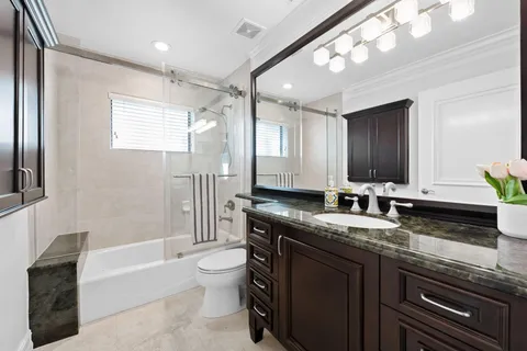 a bathroom with a granite countertop sink a toilet a mirror and shower