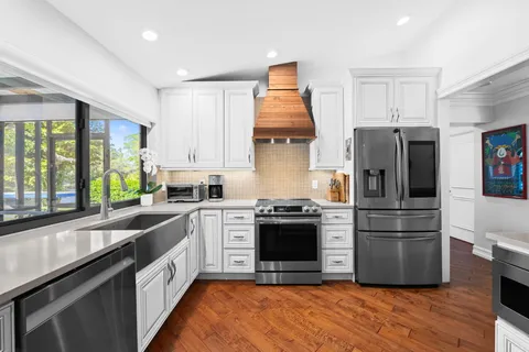 a kitchen with stainless steel appliances granite countertop a refrigerator a sink dishwasher a stove and white countertops with wooden floor