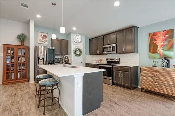 a kitchen with stainless steel appliances granite countertop a stove top oven a sink dishwasher and a refrigerator with wooden floor