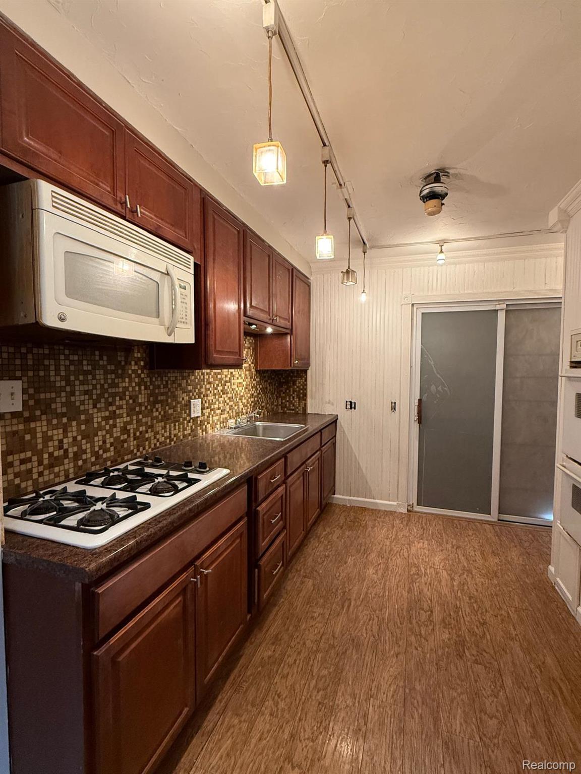 20231 Moross Road Detroit, MI 48224 - Photo 5 of 23 Kitchen with dark countertops, dark wood-type flooring, white appliances, pendant lighting, and wood walls