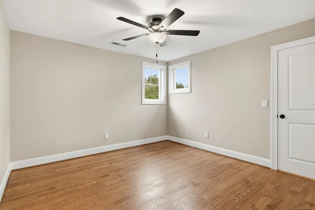 an empty room with wooden floor chandelier fan and windows