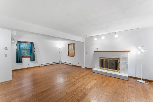 an empty room with wooden floor fireplace and windows