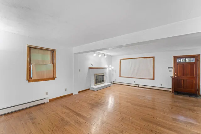 an empty room with wooden floor fireplace and windows