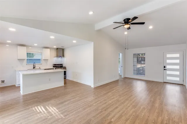 a view of an empty room and kitchen with wooden floor