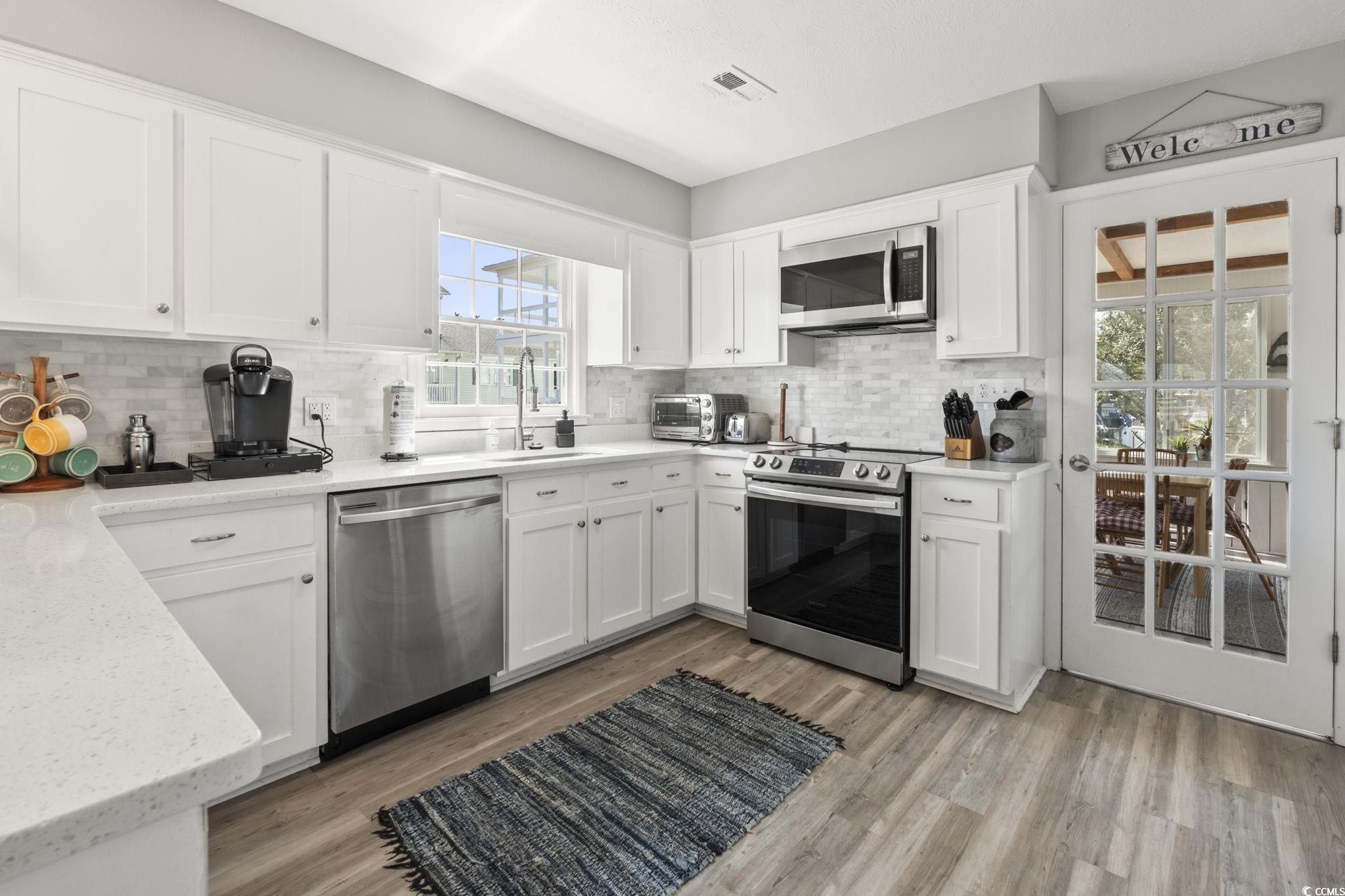 3182 State Rd S-26-816 Murrells Inlet, SC 29576 - Photo 5 of 40 Kitchen featuring appliances with stainless steel finishes, white cabinets, light wood finished floors, and tasteful backsplash
