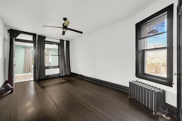 a view of an empty room with wooden floor and a ceiling fan