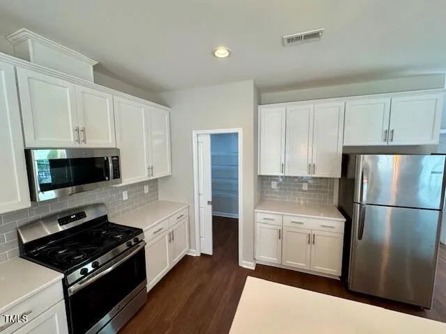 a kitchen with stainless steel appliances a refrigerator stove and white cabinets