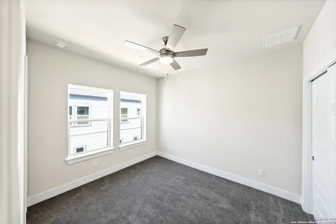 an empty room with chandelier fan and windows