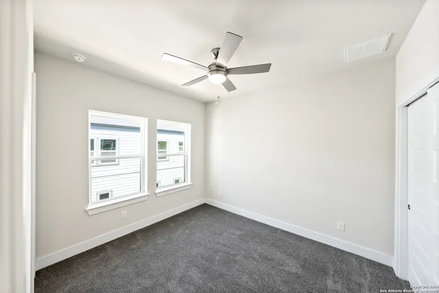 an empty room with chandelier fan and windows