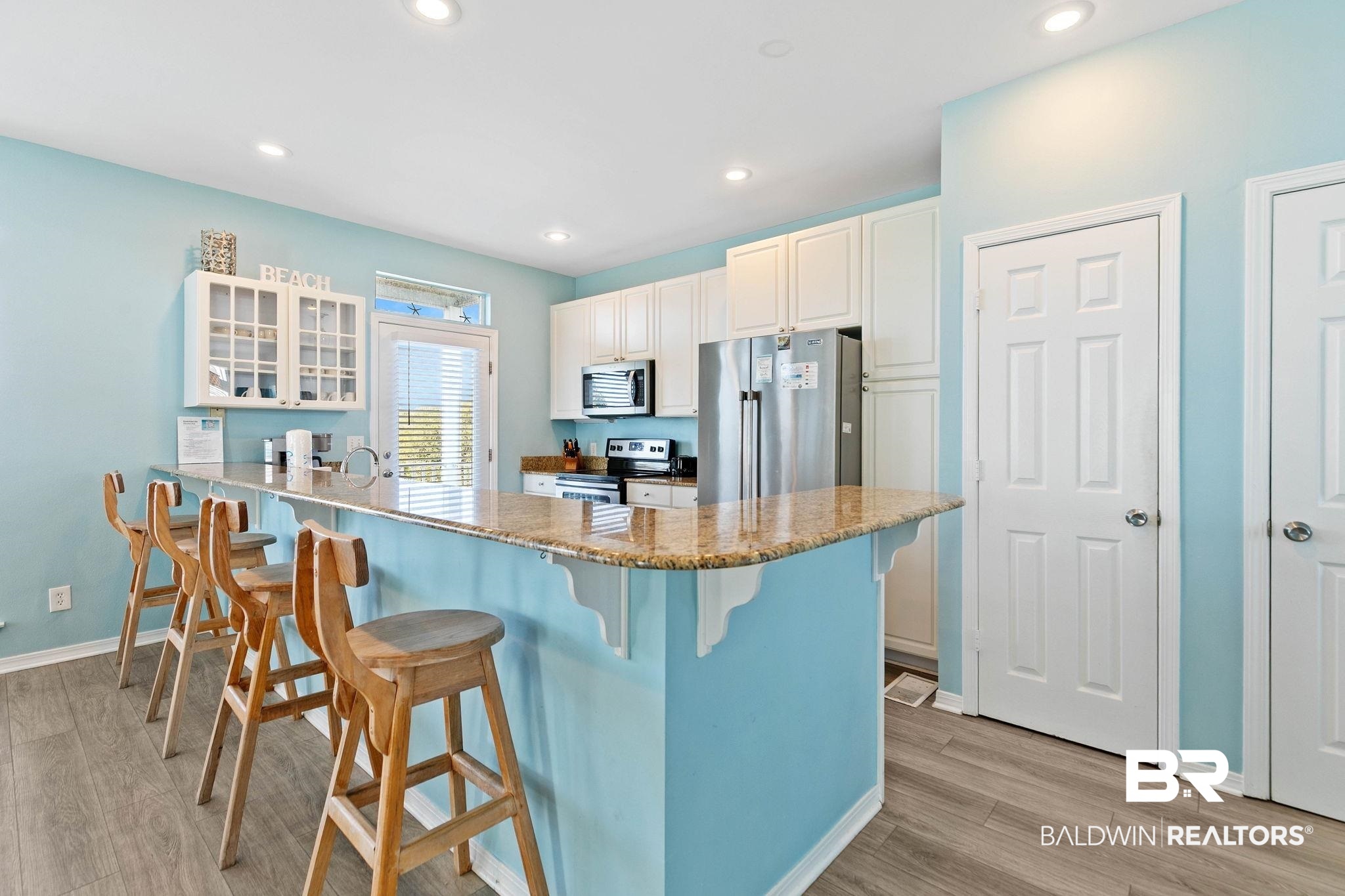 545 Plantation Road, Unit 3 Gulf Shores, AL 36542 - Photo 12 of 54 Kitchen with a peninsula, light stone counters, a kitchen bar, glass insert cabinets, and appliances with stainless steel finishes