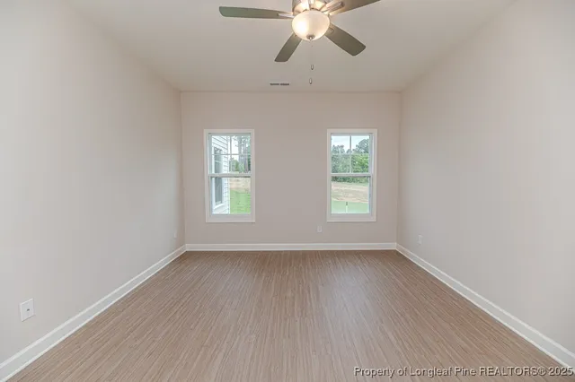 an empty room with wooden floor fan and windows