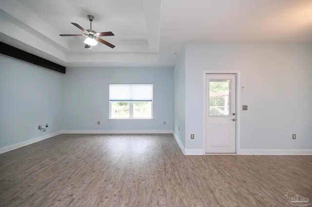 an empty room with wooden floor chandelier fan and windows
