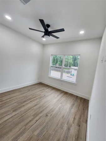 an empty room with wooden floor fan and windows