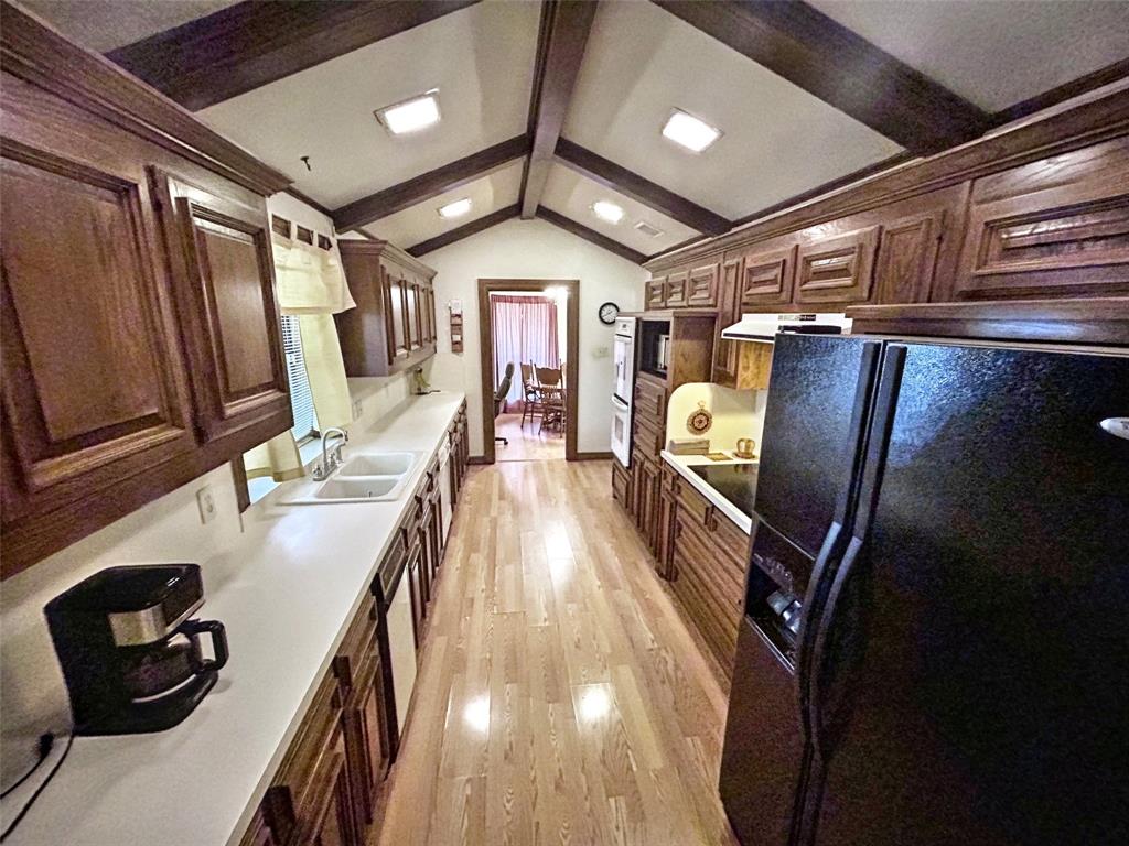 4905 Rippy Road Flower Mound, TX 75028 - Photo 24 of 29 Kitchen with black appliances, light wood-style floors, a sink, range hood, and light countertops