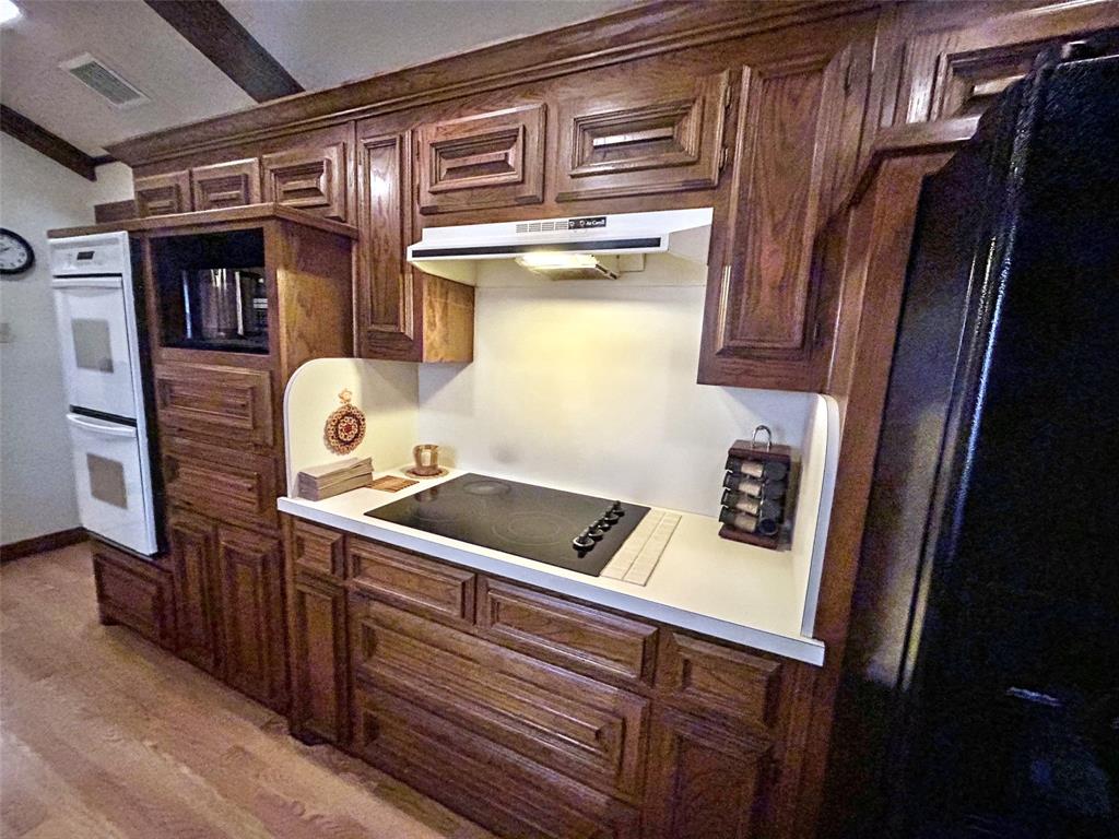 4905 Rippy Road Flower Mound, TX 75028 - Photo 25 of 29 Kitchen with under cabinet range hood, black electric cooktop, white double oven, light wood-style flooring, and light countertops