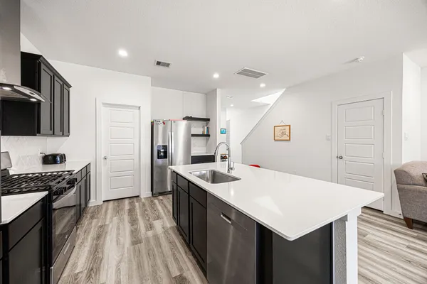 a kitchen with stainless steel appliances a sink dishwasher a stove top oven a refrigerator with island and chairs