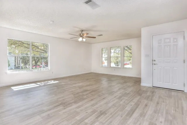 an empty room with wooden floor chandelier fan and windows