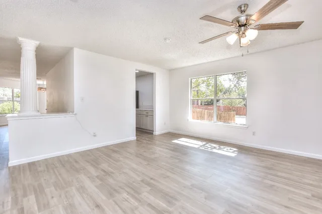 an empty room with wooden floor chandelier fan and windows