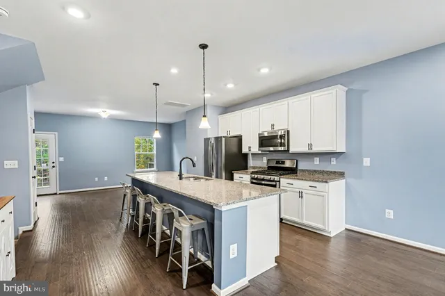 a kitchen with stainless steel appliances granite countertop a stove top oven a sink a refrigerator and white cabinets with wooden floor