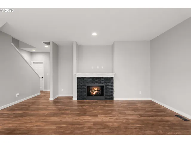 a view of an empty room with wooden floor fireplace and a window