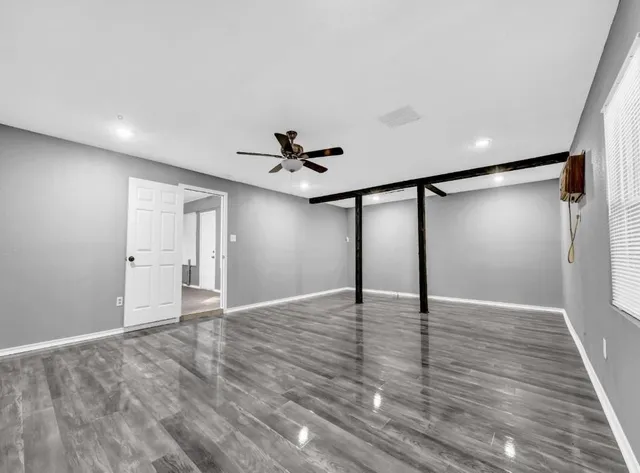 a view of an empty room with wooden floor and a ceiling fan