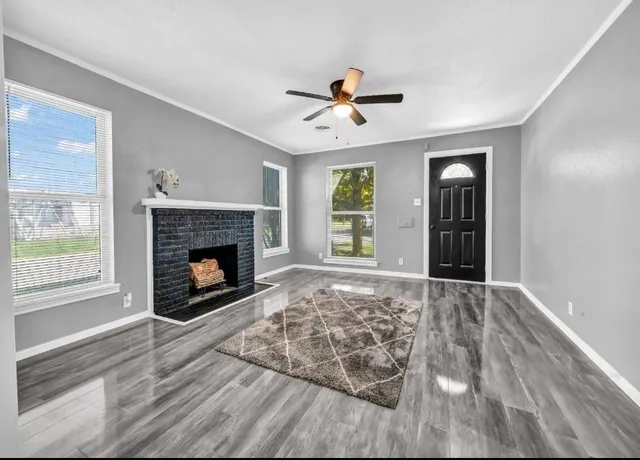 a view of an empty room with wooden floor fireplace and a window