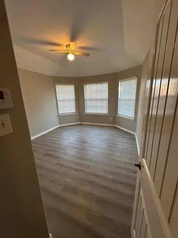 a view of an empty room with wooden floor and fan