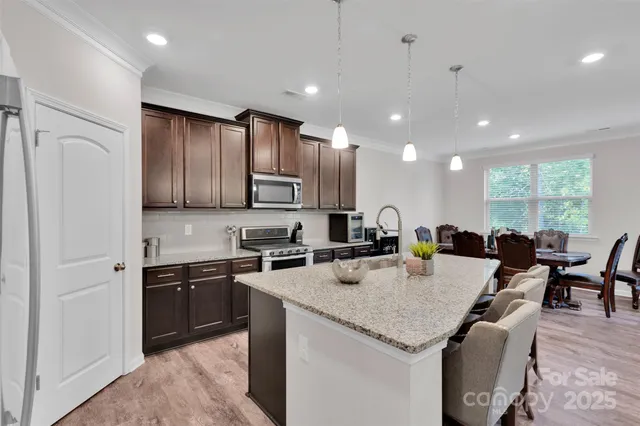 a kitchen with stainless steel appliances granite countertop a refrigerator a stove top oven a sink dishwasher a dining table and chairs with wooden floor