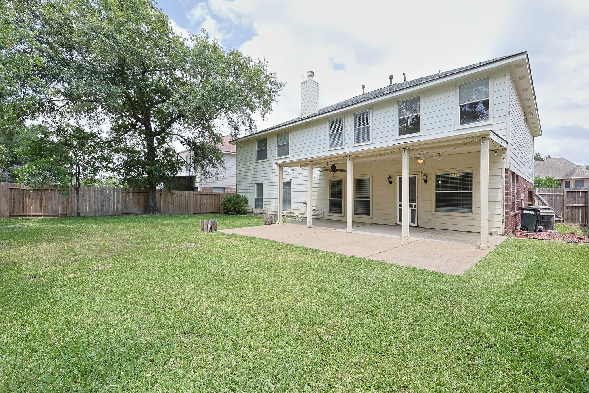 23019 Eastgate Village Drive Spring, TX 77373 - Photo 42 of 46 Spacious backyard with a well-maintained lawn, featuring a large covered patio attached to a two-story house. The area is fenced, offering privacy and a mature tree provides shade. Ideal for outdoor activities and entertaining.