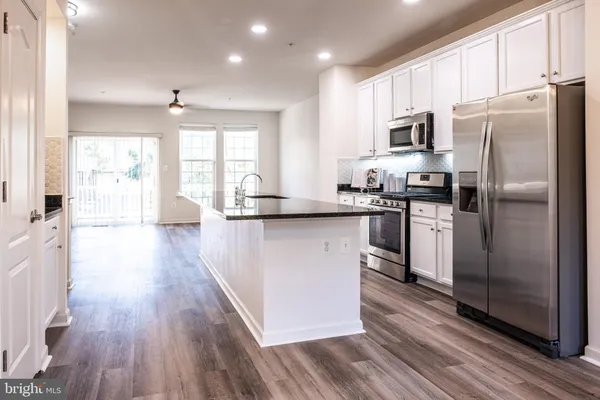a kitchen with stainless steel appliances a microwave a stove a sink dishwasher a refrigerator and white cabinets with wooden floor