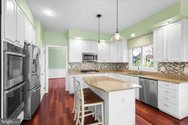a kitchen with stainless steel appliances granite countertop a sink a stove a refrigerator and island with wooden floor