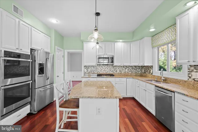 a kitchen with stainless steel appliances granite countertop a refrigerator a sink dishwasher a stove and white cabinets with wooden floor