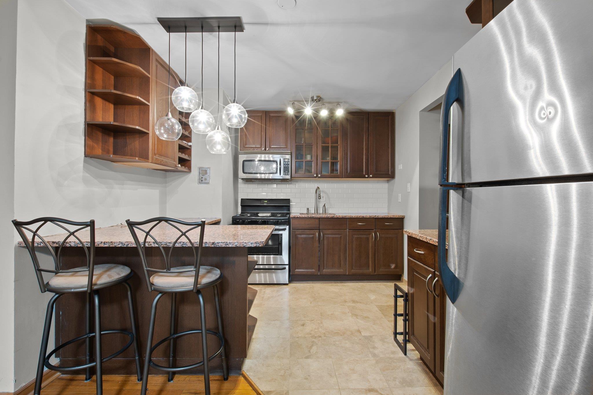 100-11 67th Road, Unit 408 Queens, NY 11375 - Photo 1 of 1 Kitchen featuring tasteful backsplash, a kitchen breakfast bar, glass insert cabinets, stainless steel appliances, and a sink