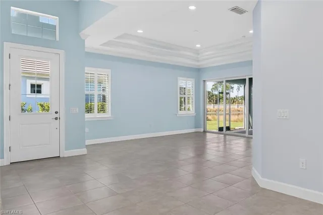 an empty room with windows and view of kitchen